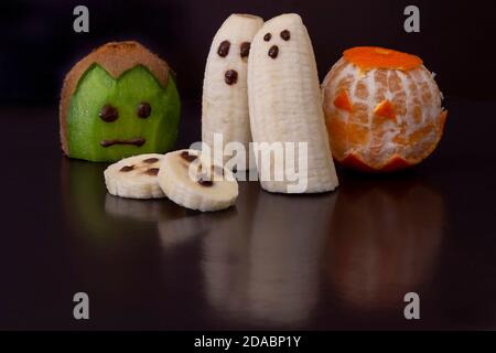 Kleine niedliche halloween-Stil Monster und Geister aus geschnitten Obst und dekoriert auf reflektierendem, glänzendem schwarzem Hintergrund Stockfoto