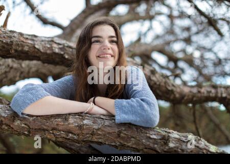 Teenager-Mädchen in Baumzweigen, lächelnd mit Sommersprossen und langen Haaren Stockfoto