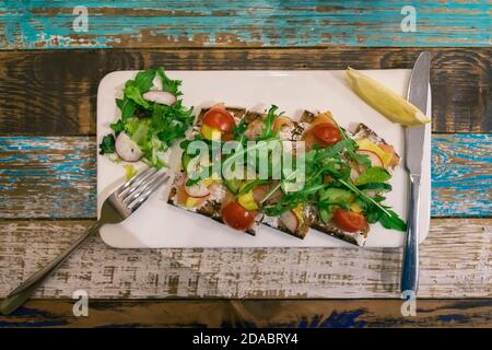 Holztisch mit weißem Teller mit frischem Gemüsesalat, Gabel, Messer, Draufsicht, Vintage-Stil Stockfoto