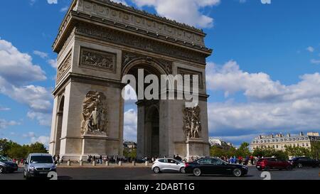 Paris, Frankreich - 09/08/2019: Blick auf das berühmte Denkmal Arc de Triomphe mit Verkehr auf der umliegenden Straße und Menge von Touristen an sonnigen Tag im Herbst. Stockfoto