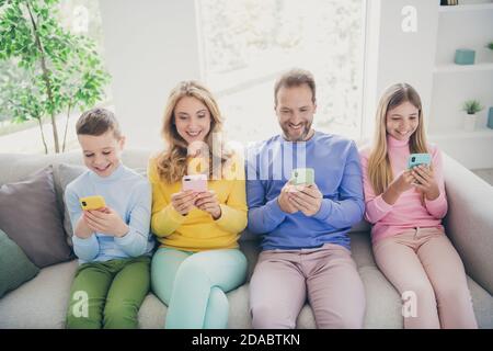 Ganzkörper-Foto von positiven Familienmenschen sitzen Sofa Mama Papa zwei kleine Kinder nutzen Smartphone im Haus drinnen Stockfoto