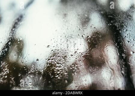 Verschwommenes Spiegelbild der Straße in einem Nebelfenster, Wassertropfen nach Regen fließen ins Glas. Wassertropfen auf dem Fenster. Konzept für Regentage. Stockfoto