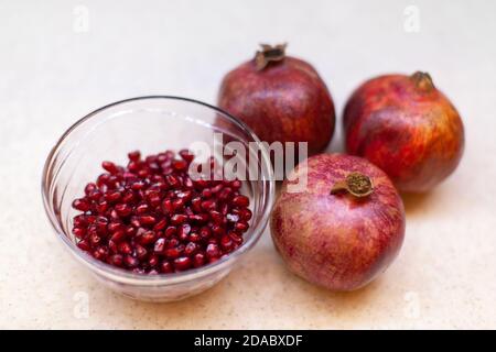 Drei reife Granatäpfel, eine Schüssel mit roten Samen auf einem hellen Tisch, Nahaufnahme. Gesundes Lifestyle-Konzept, Veganismus, Vegetarismus, Essen. Horizontales Format. Stockfoto