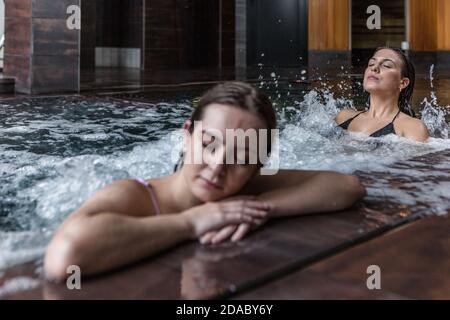 Junge Freundinnen entspannen beim Baden im Spa-Pool mit Hydromassage während der Freizeit im Luxus-Wellness-Club Stockfoto