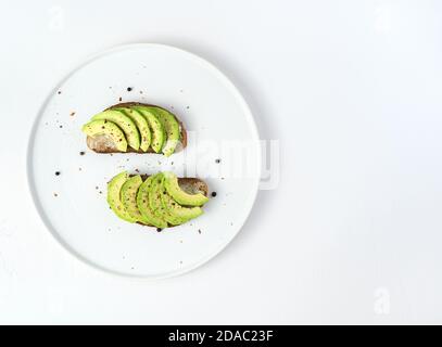 Zwei Avocado- und Roggenbrot-Sandwiches in einem weißen Gericht auf weißem Hintergrund. Stockfoto
