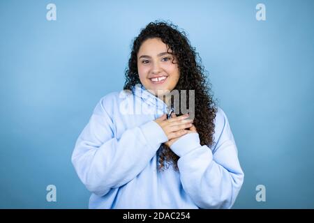 Junge schöne Frau trägt lässige Sweatshirt über isolierten blauen Hintergrund lächelnd mit ihren Händen auf der Brust und dankbare Geste auf ihrem Gesicht.