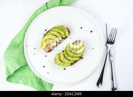 Kulinarischer Hintergrund mit Avocado-Sandwiches auf weißem Hintergrund mit Besteck und Serviette. Stockfoto