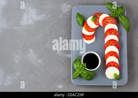 Weihnachtlicher Caprese-Salat in Form von Zuckerrohr. Mozzarella und Tomate auf grauem Teller serviert für Neujahr auf steinernem Hintergrund Stockfoto