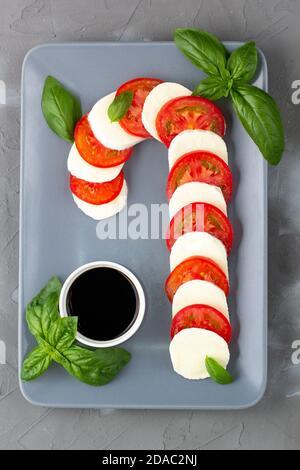 Weihnachtlicher Caprese-Salat in Form von Zuckerrohr. Mozzarella und Tomate auf grauem Teller serviert für Neujahr auf steinernem Hintergrund Stockfoto