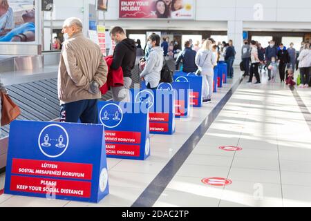 Antalya, Türkei-circa Okt, 2020: Passagiere warten auf Gepäck, ohne eine soziale Distanz zu halten. Hinweistafeln, die sie auffordern, einen sozialen dist zu halten Stockfoto