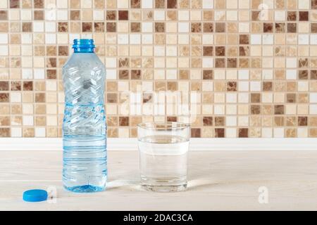 Glas reines Trinkwasser und halb volle blaue Plastikflasche auf einem weißen Holztisch. Durst löschen und Gesundheitskonzept. Speicherplatz kopieren. Vorderansicht. Stockfoto