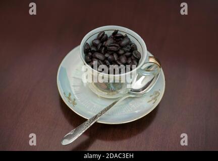 Eine Tasse für türkischen Kaffee oder Espresso, gefüllt mit Kaffeebohnen, auf seinem kleinen Teller und seinem silbernen Löffel. Stockfoto
