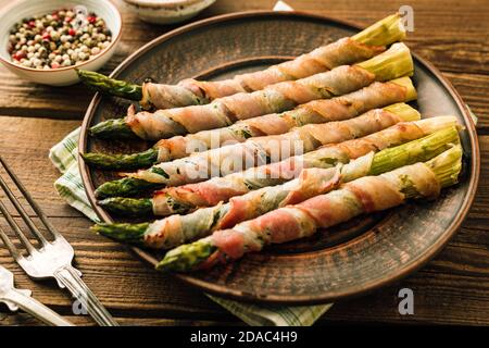 Spargeltriebe in Speck gebacken. Snack auf Holzhintergrund Stockfoto