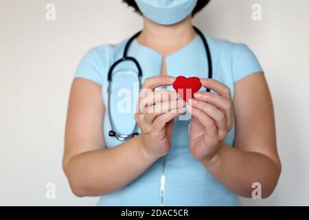 Leben retten während einer Covid-19-Coronavirus-Pandemie, Ärztin in medizinischer Maske hält rot gestricktes Herz in den Händen Stockfoto