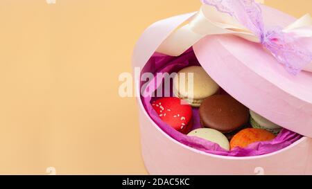 Vier farbenfrohe französische Macarons in rosa Pappkarton auf pfirsichfarbenem Hintergrund. Stockfoto