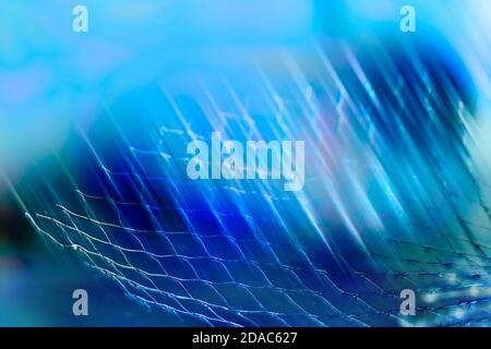 Künstlerisch blau getönten Hintergrund. Abstrakte Netzdetails und leichte Streifen. Nahaufnahme von glänzendem Metall-, Kunststoff- oder Textilgewebe in cooler, frischer Gitterstruktur. Stockfoto