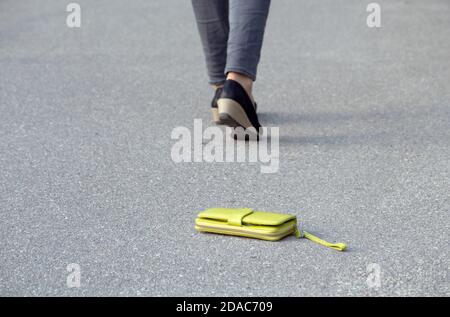 Frau verlor Geldbörse auf der Straße. Nur ihre Beine gehen weg im Bild, allgemeine Fokus auf die Brieftasche. Stockfoto