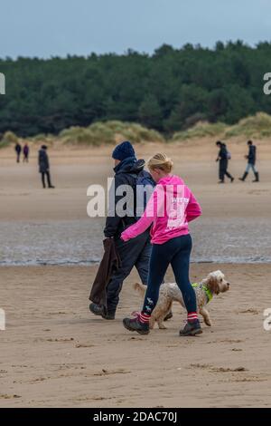 Ein Mann und eine Frau, Vater und Tochter, die einen Hund am Strand in norfolk an einem Sandstrand in holkham laufen. Stockfoto