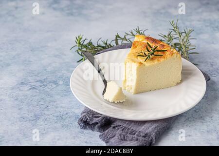 Käsekuchen mit Zitronenvanille, verziert mit Rosmarin-, Minze- und Zitronenscheiben. Ricotta keine Kruste Käsekuchen oder Kasserolle. Blauer Betonhintergrund. Stockfoto