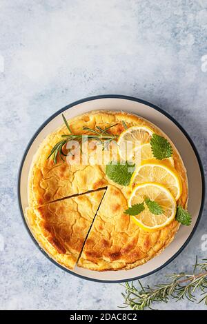 Käsekuchen mit Zitronenvanille, verziert mit Rosmarin-, Minze- und Zitronenscheiben. Ricotta keine Kruste Käsekuchen oder Kasserolle. Blauer Betonhintergrund. Draufsicht. Stockfoto