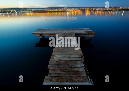 Leerer Angelpier bei Nacht mit der Stadt im Hintergrund mit Orange und blauem Grün Stockfoto
