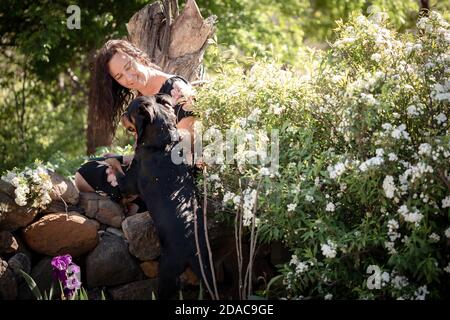 Frau sitzt auf einer Steinmauer in einem schönen Ferienhaus Garden patting a rottweiler Hund Stockfoto