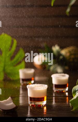 Tropische alkoholische Aufnahmen mit Kokosflocken, Monstera Blume mit Kokosnuss und Ananas auf braunem Holzhintergrund dekoriert Stockfoto