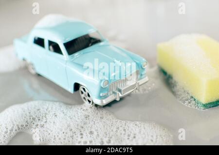 Autowaschszene mit kleiner Serienproduktion Spielzeugmodell des sowjetischen beliebten Oldtimers Wolga GAZ-21, gelber Schwamm, Schaumstoff um auf grauem Hintergrund. Stockfoto