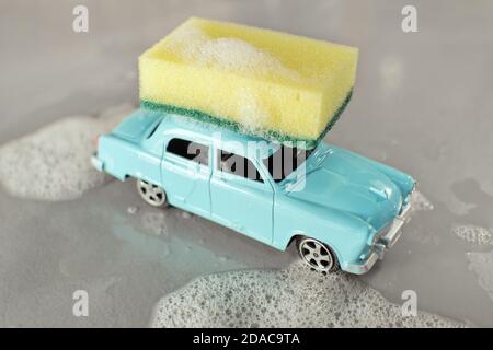 Autowaschszene mit kleiner Serienproduktion Spielzeugmodell des sowjetischen beliebten Oldtimers Wolga GAZ-21, gelber Schwamm, Schaumstoff um auf grauem Hintergrund. Stockfoto