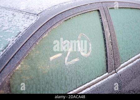 Gefrorenes Autofenster mit zerkratztem Text auf dem Eis: '-20' (minus zehn) und Reinigungswerkzeug Stockfoto