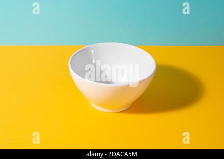 Leere weiße Keramikschale auf gelbem und blauem Hintergrund Stockfoto