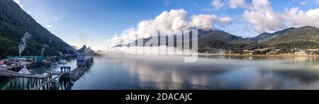 Panoramabild des Hafens von Juneau und der mit Wolken und Nebel bedeckten Berge im Gastineau Channel, Alaska. Kreuzfahrtschiff und Boote dockten im Hafen an. Blu Stockfoto