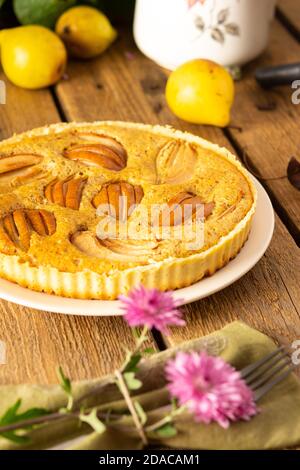 Köstlicher Birnenkuchen aus gelben Birnen auf Holzgrund, Himbeerbusch im Hintergrund, rosa Chrysanthemen in Vase, rustikaler Stil Stockfoto
