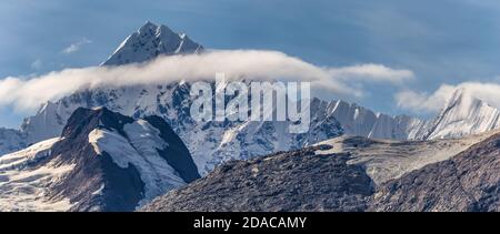 Schöne Panoramaaussicht auf einen mit Eis und Schnee bedeckten Berggipfel, umgeben von flauschigen Couds in Alaska. Blauer Himmel als Hintergrund. Stockfoto