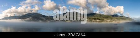 Panoramaaufnahme der mit Wolken und Nebel bedeckten Berge im Gastineau Channel, Juneau, Alaska. Goldene Stunde. Blauer wolkig Himmel als Hintergrund und Boot sa Stockfoto