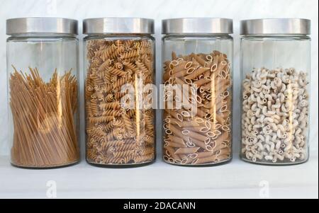 Vier große Gläser mit verschiedenen Vollkornpasta in der Küche. Stockfoto