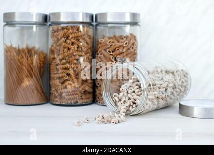 Vier große Gläser mit verschiedenen Vollkornpasta in der Küche. Glas mit Hafer cavatappi Pasta wird geöffnet und liegt. Stockfoto