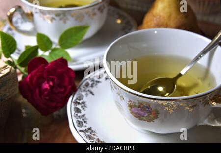 Nahaufnahme von zwei Infusionsbechern mit Vintage-Dekorationen neben einer Rose, ein paar Muffins und ein paar alte Bücher Stockfoto