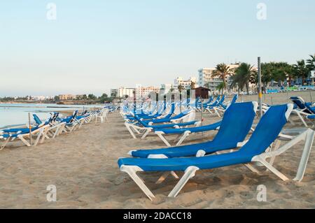 Leere blaue Sonnenliegen befinden sich am Sandstrand von Nissi. Es ist ein beliebter Strand im Resort der Ayia Napa, Zypern, Europa. Der Strand wurde mit dem blu ausgezeichnet Stockfoto