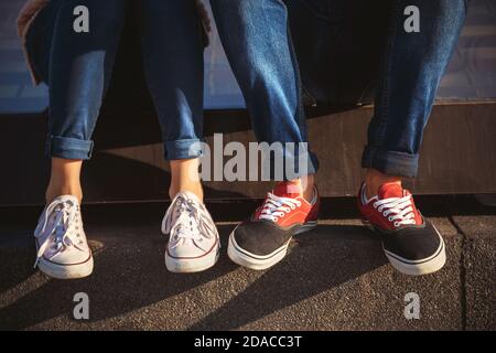 Oben Nahaufnahme von jungen Paar Beine in Turnschuhen und Jeans sitzen zusammen draußen. Stockfoto