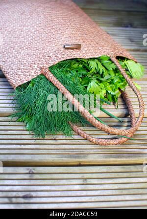 Umweltfreundliche Weidenbeutel aus natürlichen Materialien mit frischem Gemüse und Kräutern darin: Dills, grüne Zwiebel, Petersilie auf einer Holzoberfläche. Stockfoto