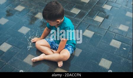 Obere Ansicht Foto eines kaukasischen Jungen mit Wasser spielen Auf dem Boden nach einem Regen Stockfoto