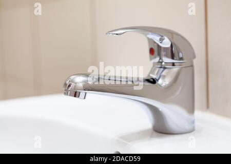 Edelstahl-Wasserhahn in einem Waschbecken, weiße Sanitär-und Wand mit beigen Fliesen Stockfoto