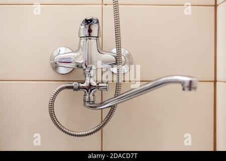 Badezimmer Wasserhahn mit langem Hals und Dusche Stahlschlauch, Wand mit beigefarbenen Fliesen Stockfoto