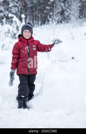 Kaukasischer Junge in roter Jacke in der Nähe Schneemann im Wald Stockfoto