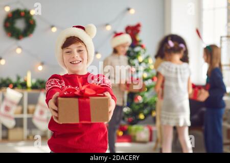 Portrait eines niedlichen lächelnden Jungen, der ein Weihnachtsgeschenk in den Händen hält und es im Wohnzimmer gibt. Stockfoto