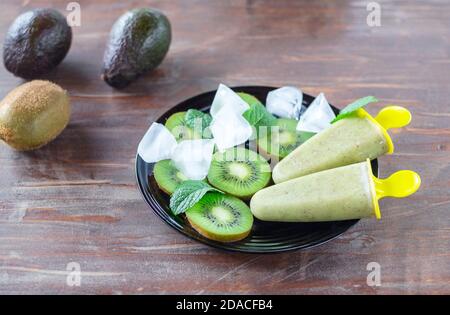 Hausgemachtes gesundes Sorbet (Fruchteis) aus Avocado und Kiwi auf dem schwarzen Teller unter Kiwi-Stücken, Minzblättern, Eiswürfeln auf dem alten Tisch Stockfoto