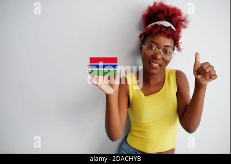 Afrikanische Frau mit afro Haar, tragen gelbe Singlet und Brillen, halten Sie die Gambia-Flagge isoliert auf weißem Hintergrund, zeigen Daumen nach oben. Stockfoto