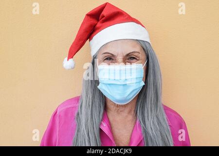 Glückliche ältere Frau trägt weihnachtsmütze mit schützenden Gesichtsmaske - Fokus auf Gesicht Stockfoto