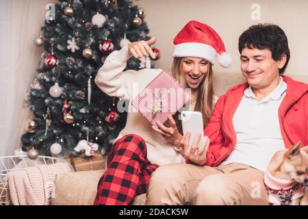 Portrait von schönen Paar Mann und Frau in rot Weihnachtsmann hat mit einem Videoanruf oder Selfie mit ihrem Smartphone, genießen sie weihnachtszeit zu Hause Stockfoto